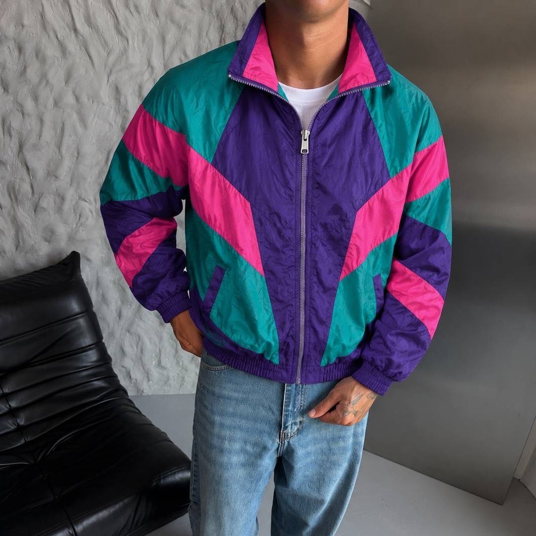 80s Windbreaker Outfit: 8 Street Looks Revived for 2026 2 A person wearing a vibrant teal, purple, and pink color-blocked windbreaker jacket and blue jeans.