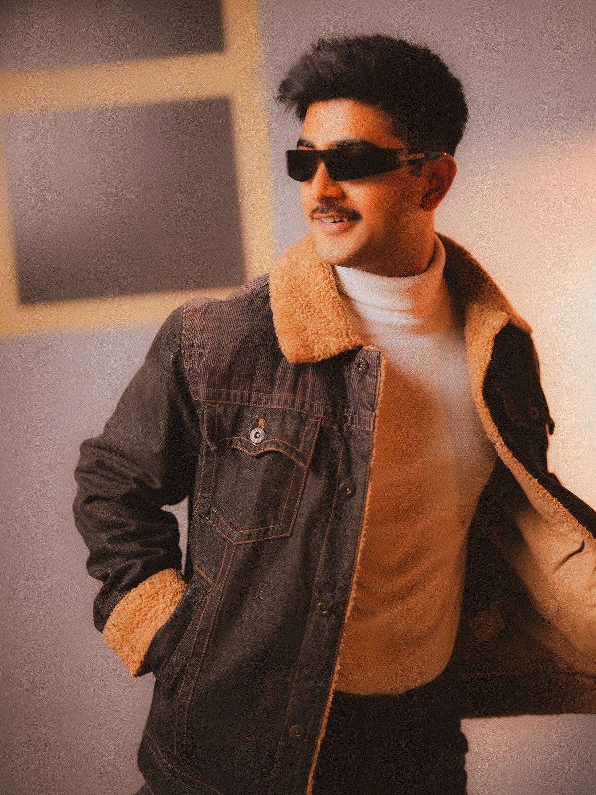 Man wearing a dark denim jacket with shearling lining over a white turtleneck sweater.