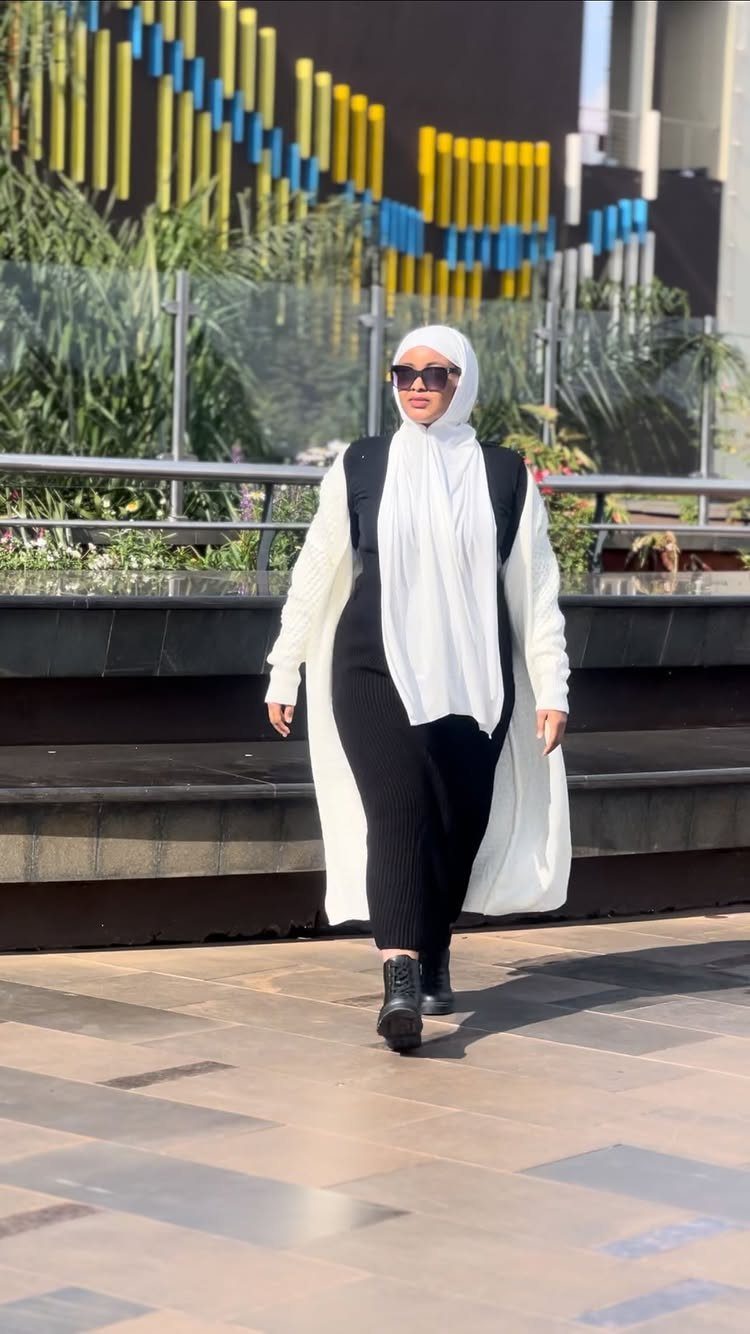 Woman in a long white cardigan and black dress walking in black ankle boots.