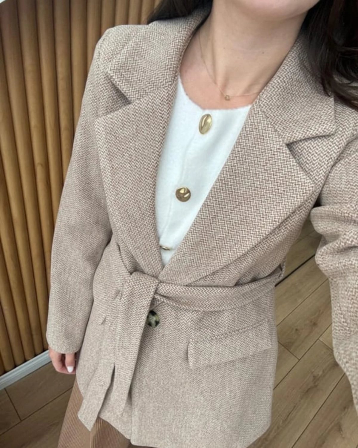 A person wearing a beige belted cashmere coat over a white buttoned top.