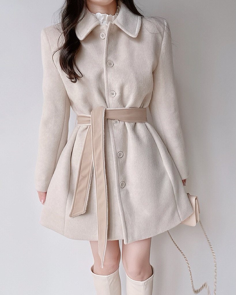 10 Winter Coat Dress Styles Worth Wearing All Season 4 A person wearing a cream belted wool coat with a flared skirt and large buttons.