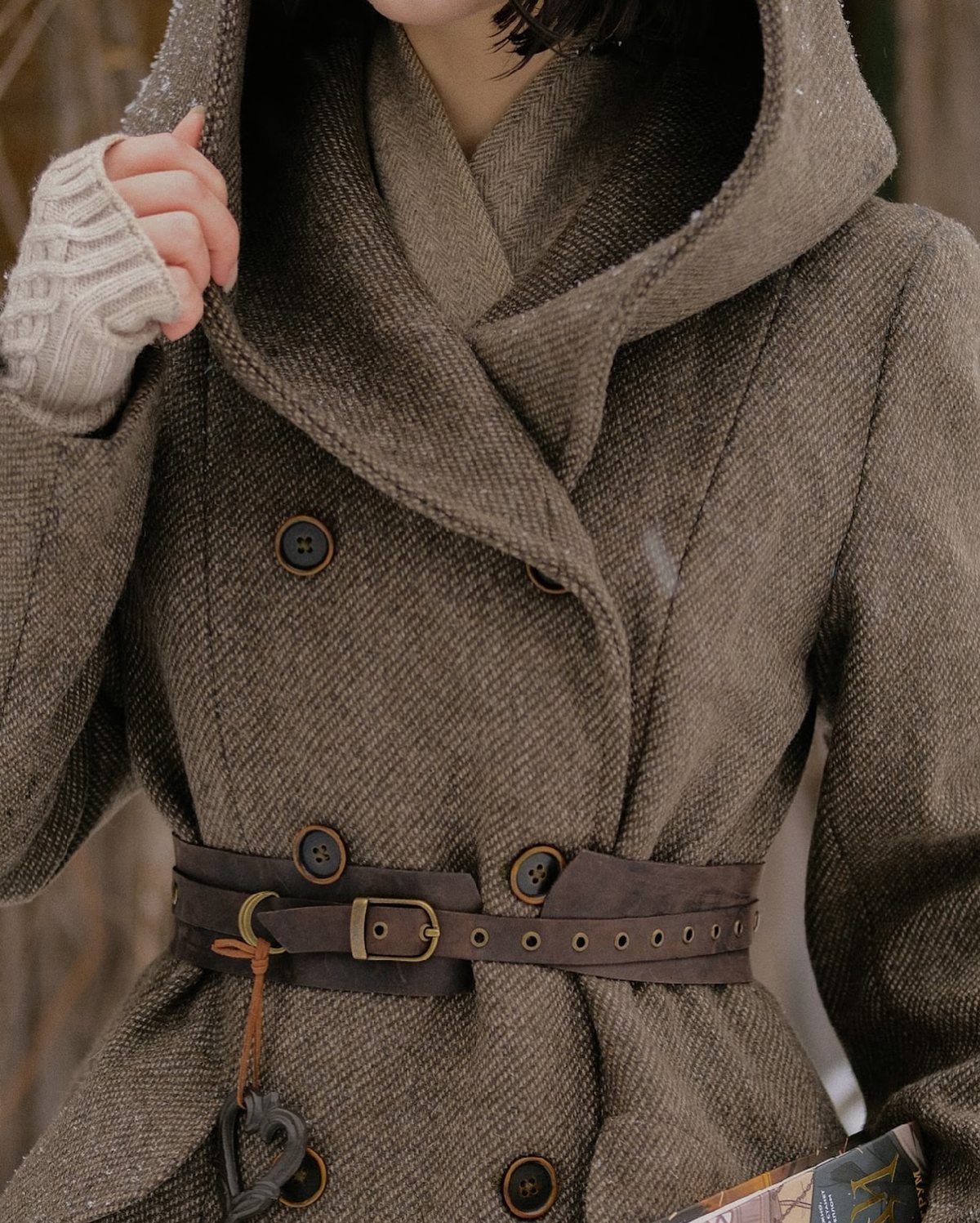 A person wearing a textured brown wool hooded coat with a leather belt.