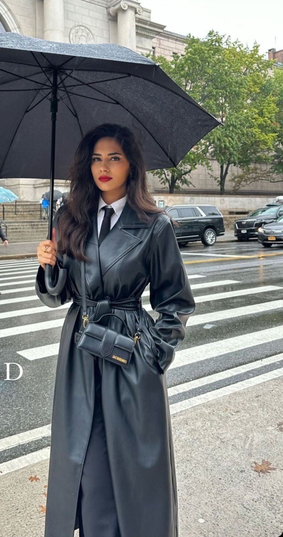 Boss Lady Outfit Ideas: 17 Looks for 2026 7 Woman in a belted black leather trench coat holding a black umbrella on a city street.