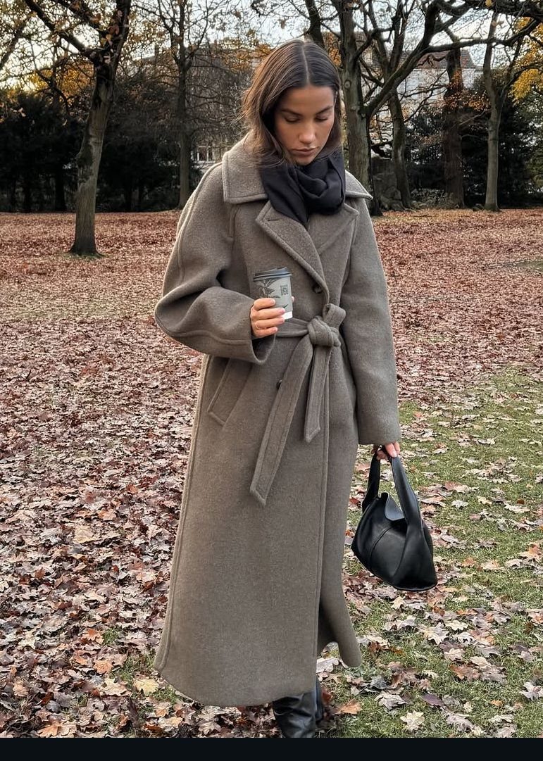 Tailored Wool Coat Styles: 8 Women's Ideas for 2026 7 A woman in a long taupe wool coat and scarf standing in a park with autumn leaves.