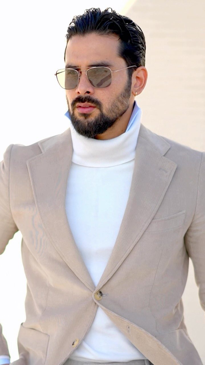 11 Blazer Outfits Casual Enough for Real Life 11 Man wearing a beige blazer over a white turtleneck sweater and sunglasses.