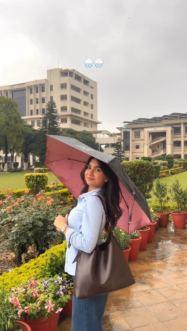 Young woman in a light blue shirt holding a large umbrella in a garden setting.