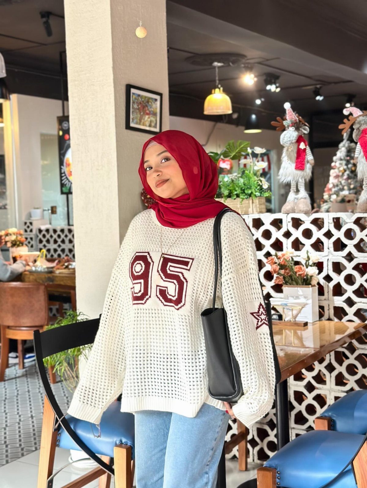 Modest Winter Outfits: 12 Ideas for Cold Days 4 Woman in a red hijab and white oversized knit sweater standing in a cafe.