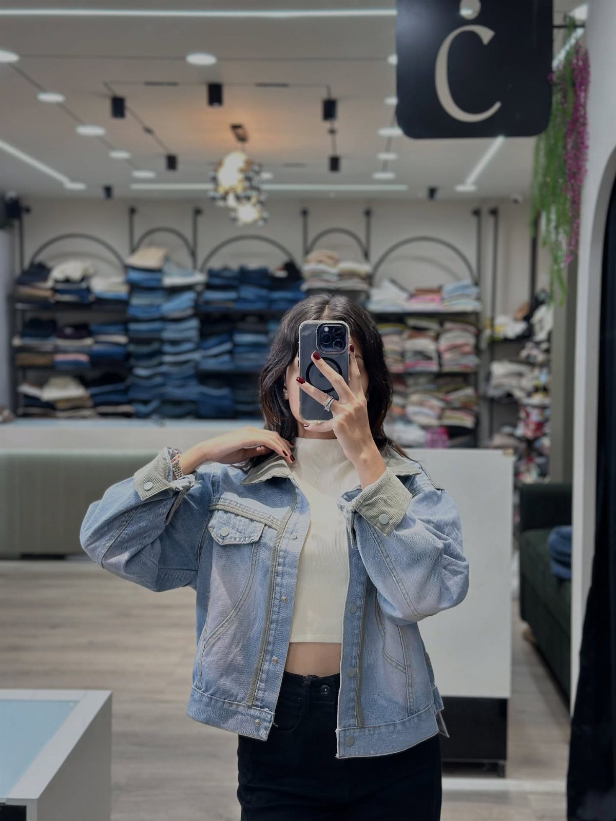 Person in a light blue denim jacket and white crop top taking a mirror selfie.
