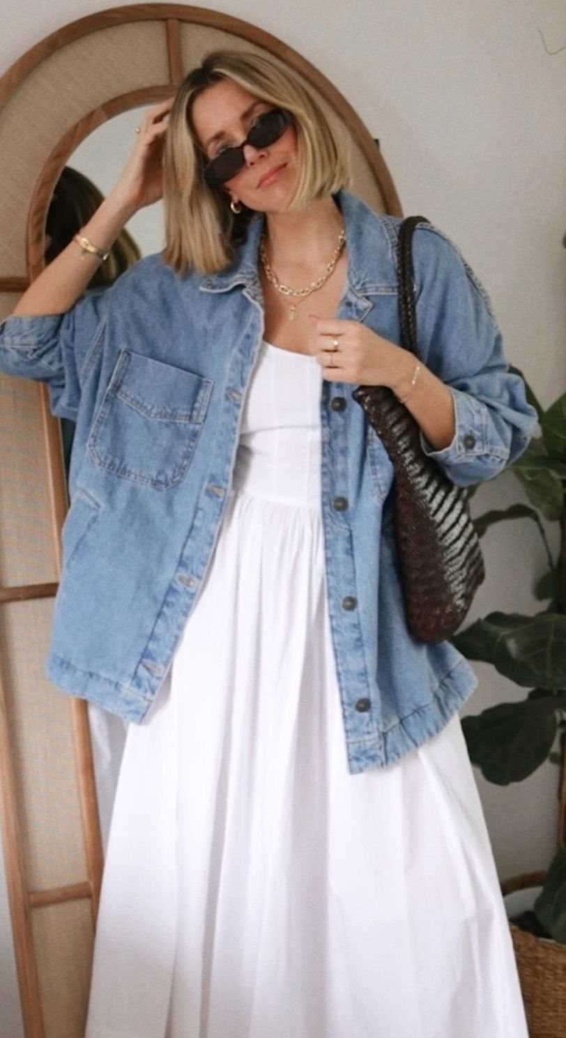 Long Denim Jacket Outfit: 8 Looks to Wear Now 3 Woman posing in a blue denim jacket layered over a long white dress.