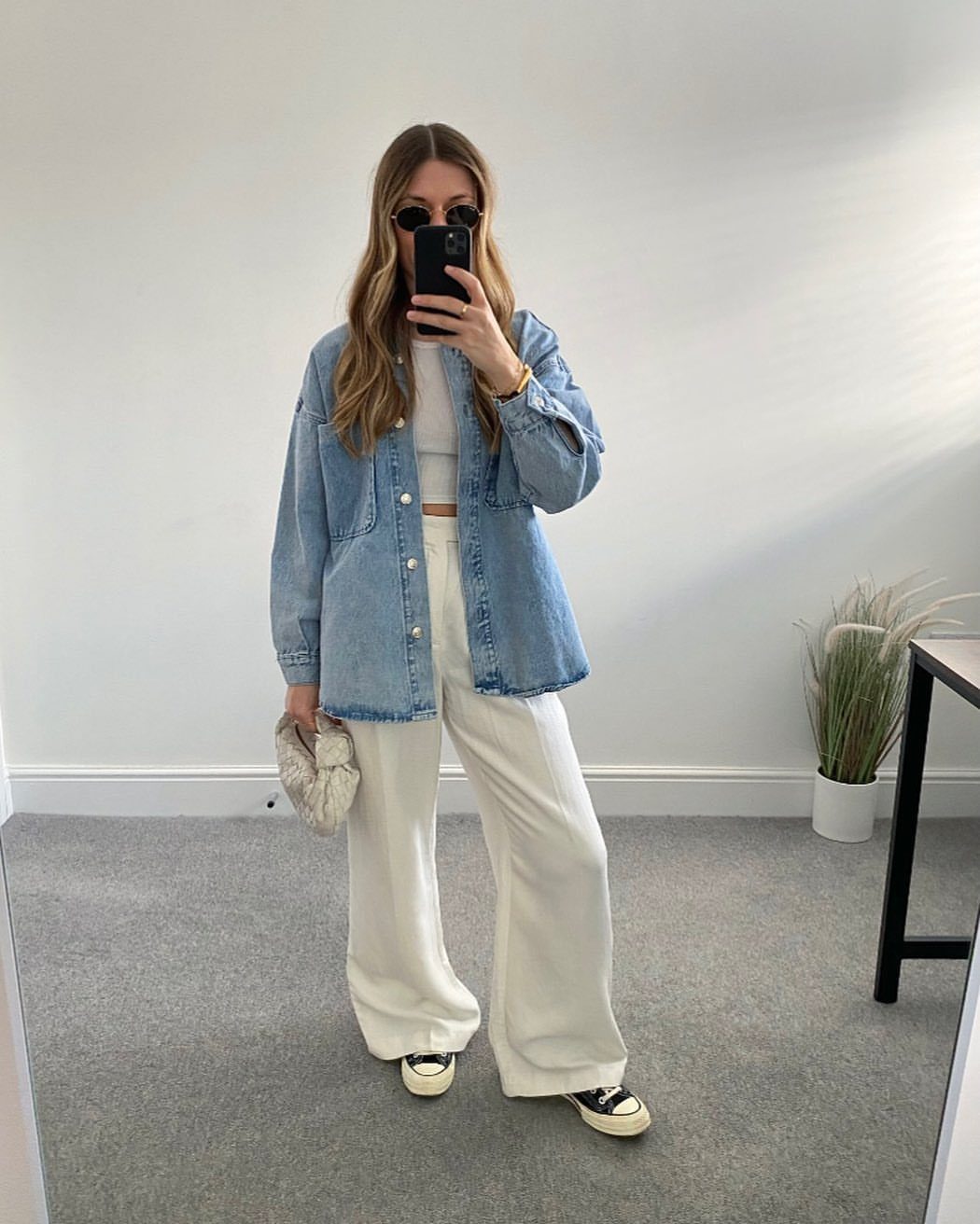 Long Denim Jacket Outfit: 8 Looks to Wear Now 6 Woman in a light blue denim jacket and white wide-leg tailored trousers posing for a mirror selfie.