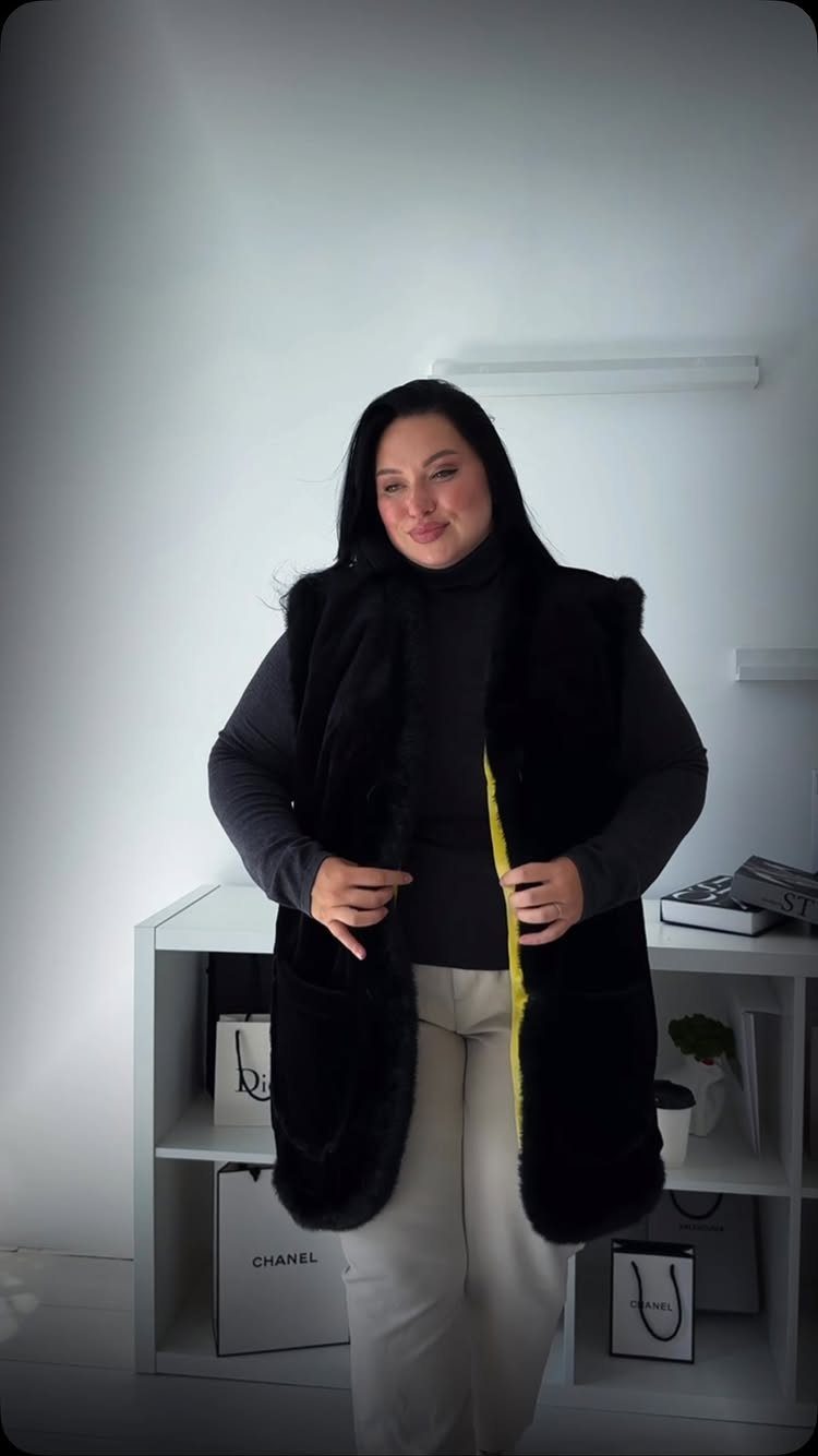 Woman wearing a black faux fur vest over a black turtleneck and light trousers.