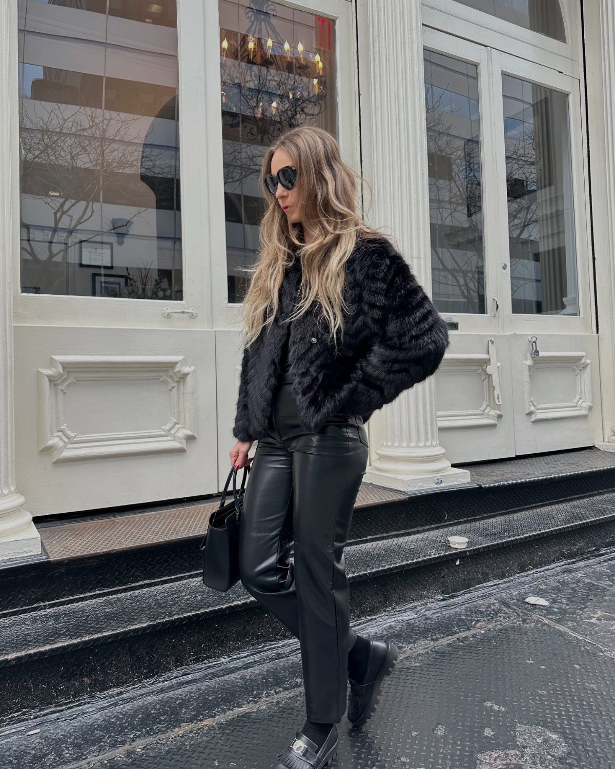 6 Winter Fashion Outfits That Make Cold Mornings Easier in 2026 5 Woman walking in black faux fur jacket and black faux leather pants outdoors.