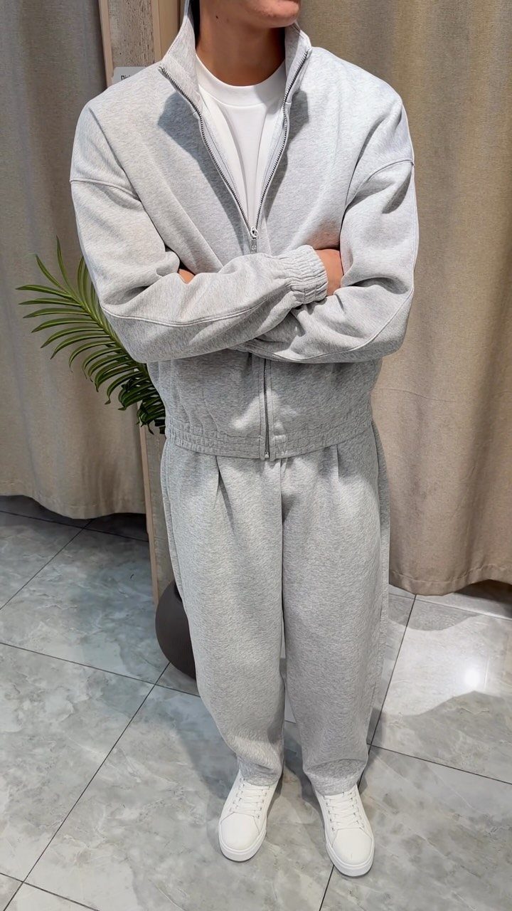 Person wearing a matching grey fleece jacket and sweatpants set with white sneakers.