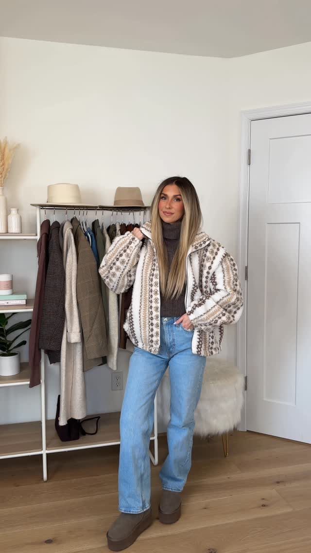 Woman wearing a patterned fleece jacket, brown turtleneck, and light blue wide-leg jeans.