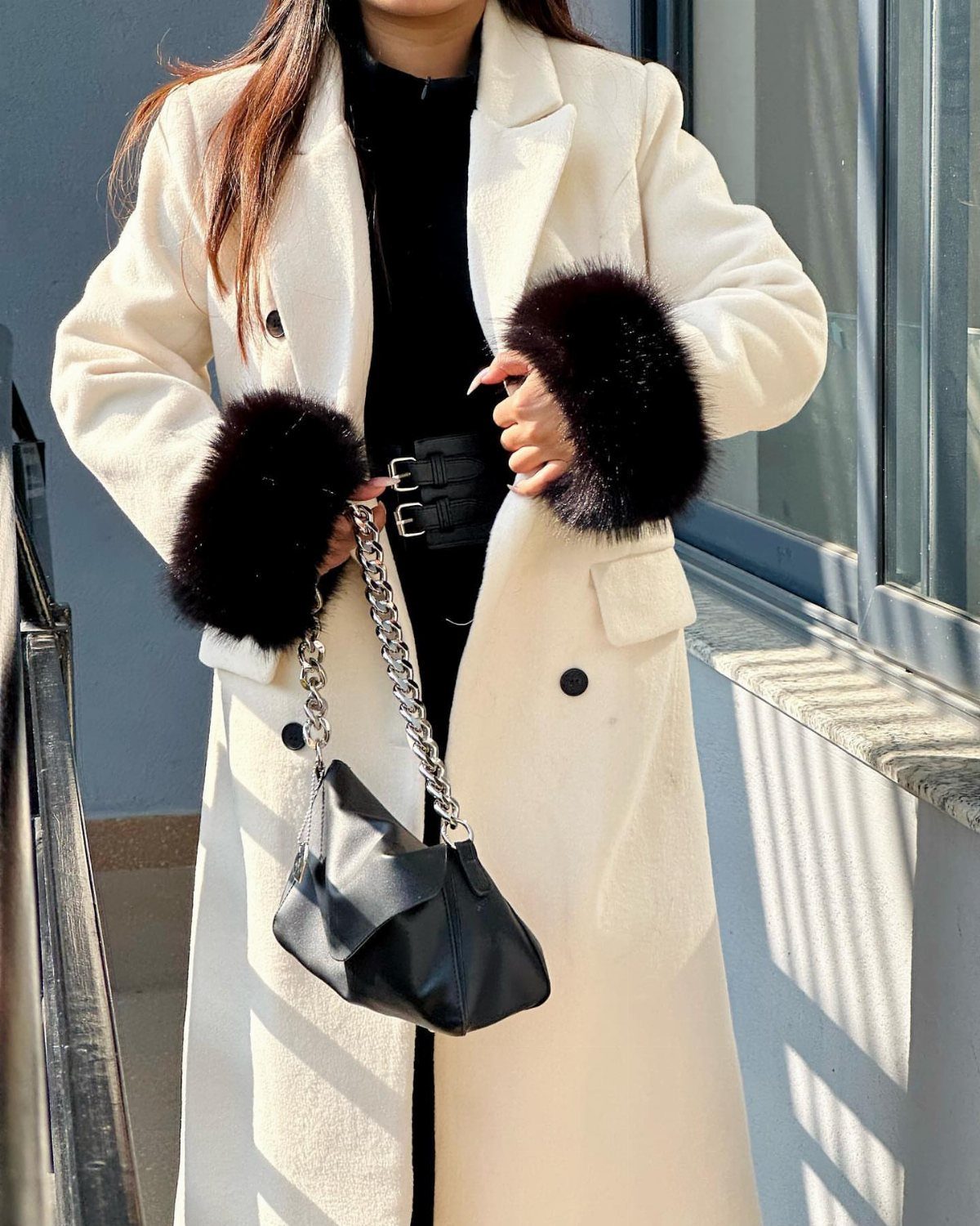 10 Winter Coat Dress Styles Worth Wearing All Season 5 A person wearing a cream coat with black fur cuffs and a black handbag.