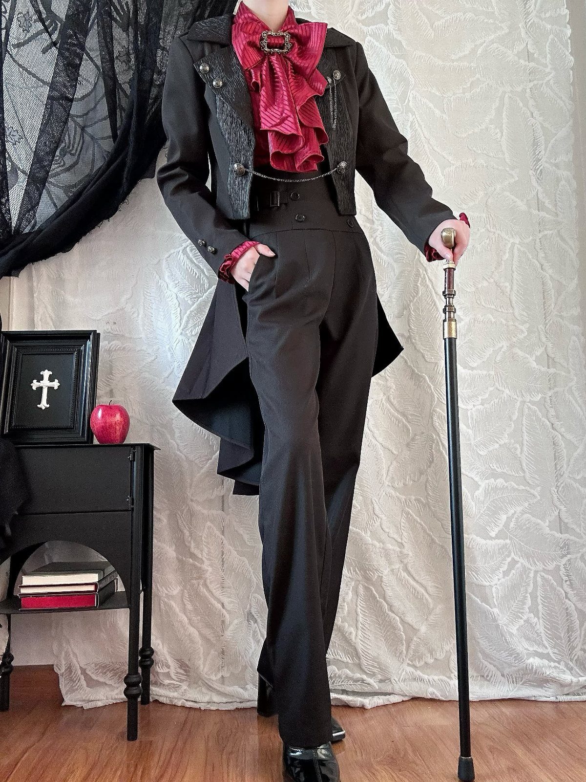Person in a black Victorian tailcoat and red ruffled shirt holding a walking cane.
