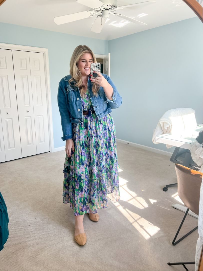 Woman posing in a mirror wearing a floral maxi dress and a blue denim jacket.