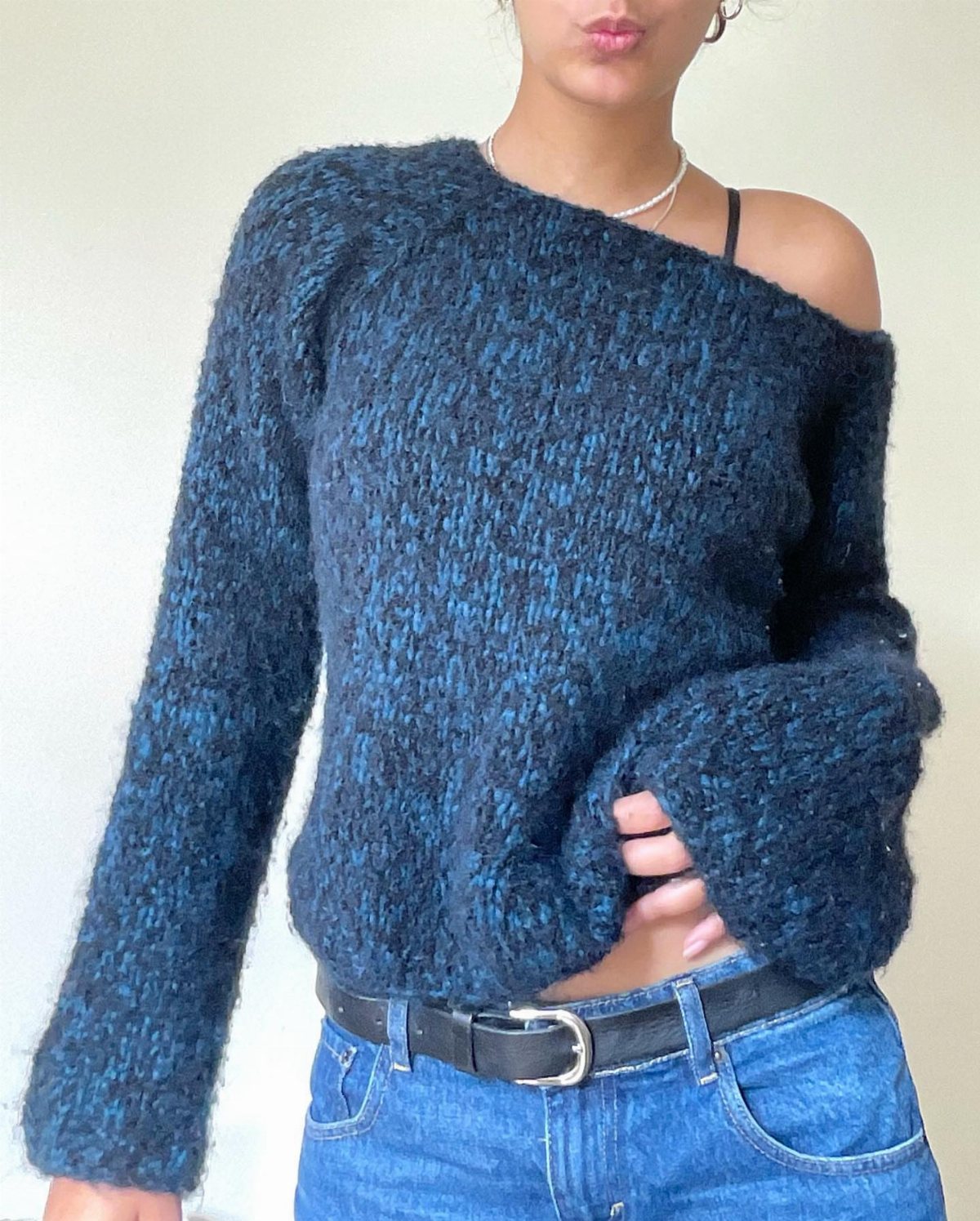 A person wearing a blue chunky knit sweater styled off one shoulder with blue jeans.