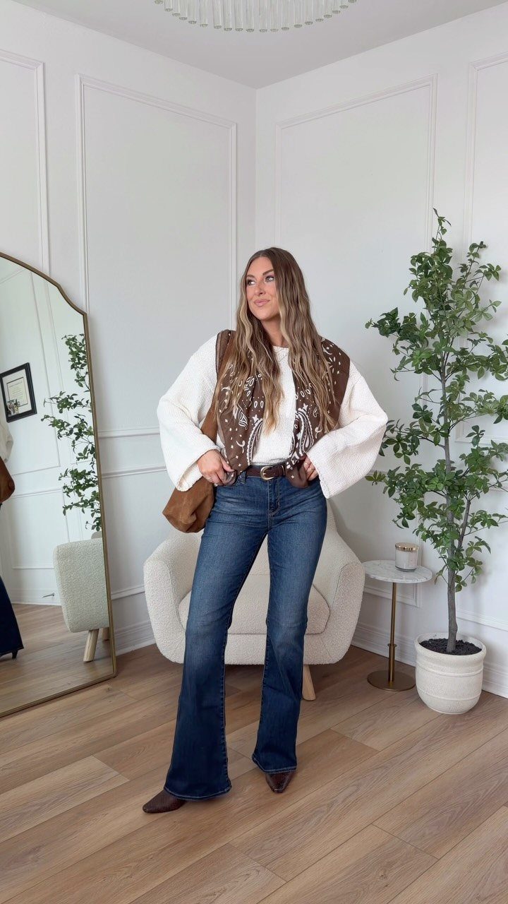 Woman wearing a white sweater, dark blue flared jeans, and a patterned brown vest.