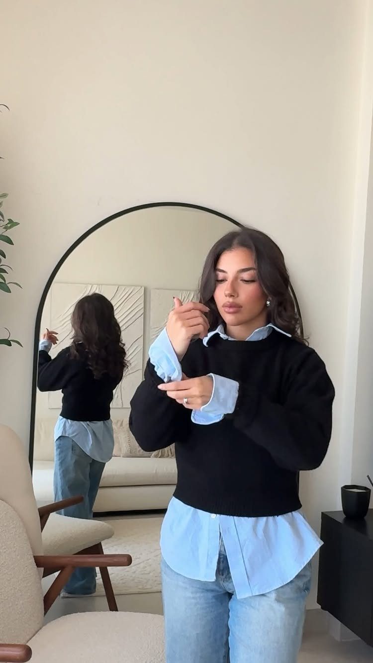 Winter Capsule Wardrobe for Women: 12 Ideas That Actually Work 2 Woman wearing a black sweater layered over a long light blue shirt and denim jeans.