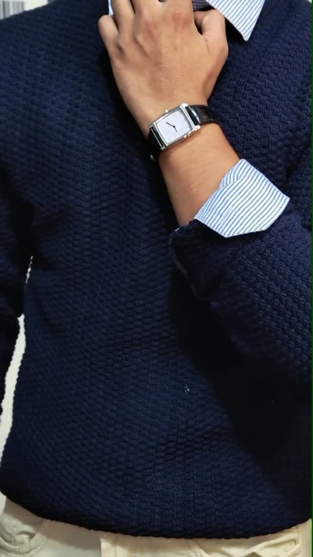 10 Knit Sweater Outfit Ideas for Fall Through Winter 2026 2 A person wearing a navy blue textured sweater over a striped collared shirt and a wristwatch.