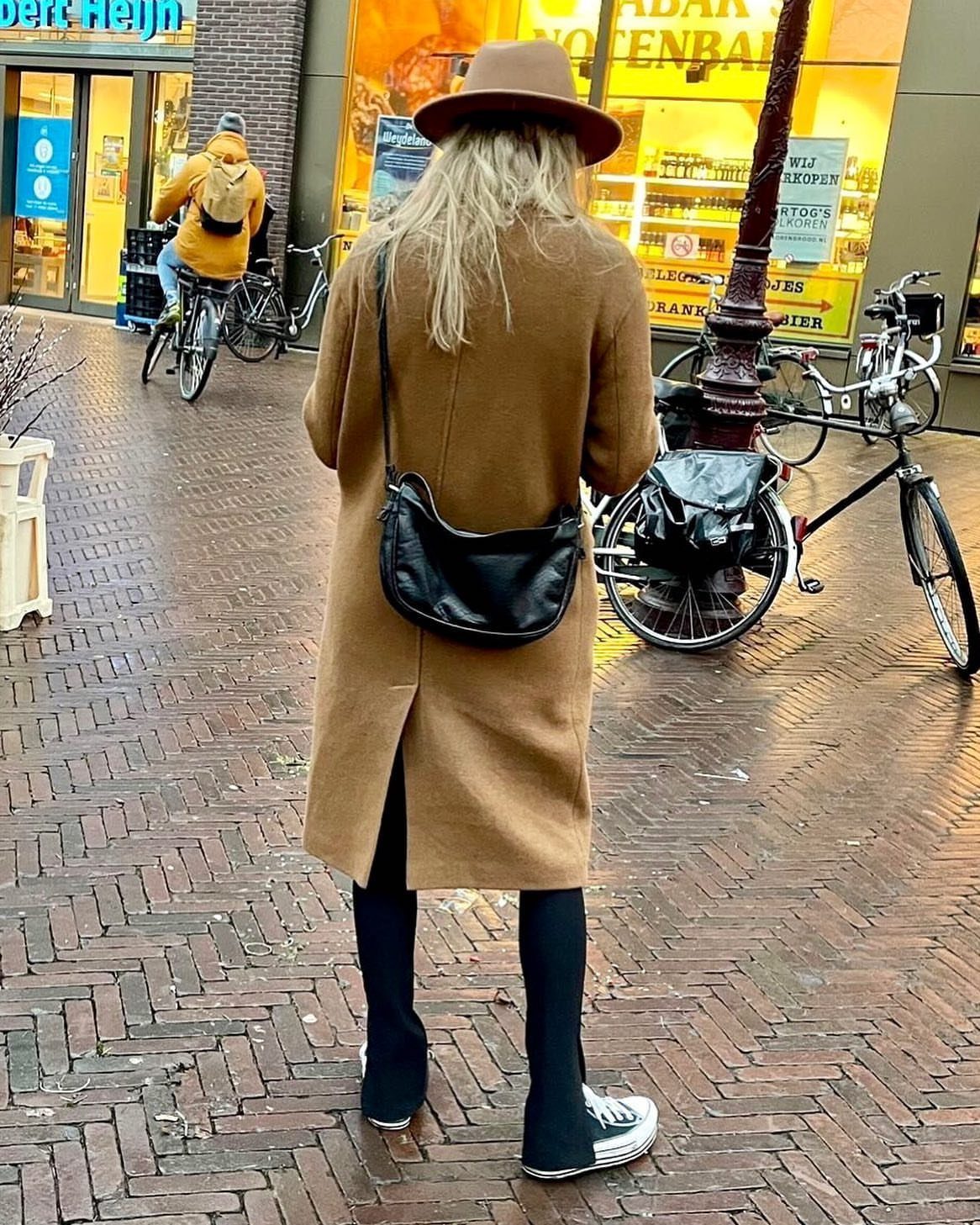 Long Jackets for Women: 8 Styles From Wool to Velvet 2 Woman from behind wearing a long camel wool coat, a brown hat, and black leggings on a brick street.