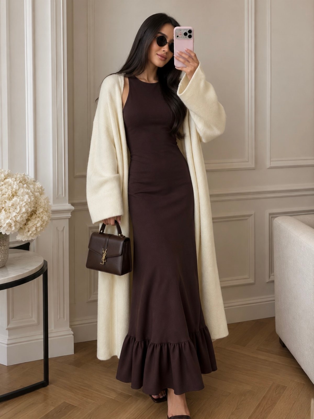 Woman in a long cream cardigan and brown maxi dress taking a mirror selfie.
