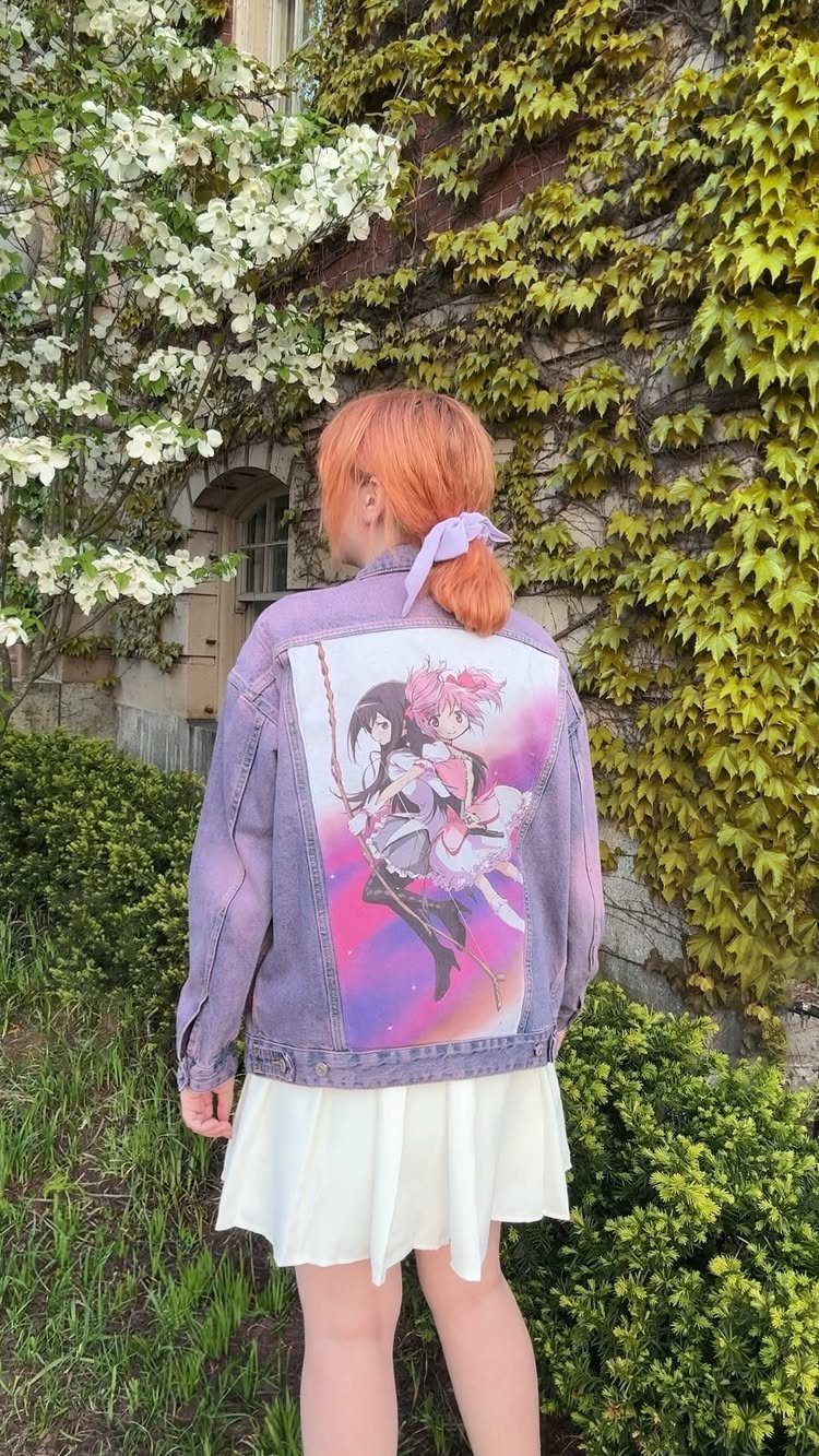 Person with orange hair wearing an oversized purple denim jacket with anime art and a white skirt.