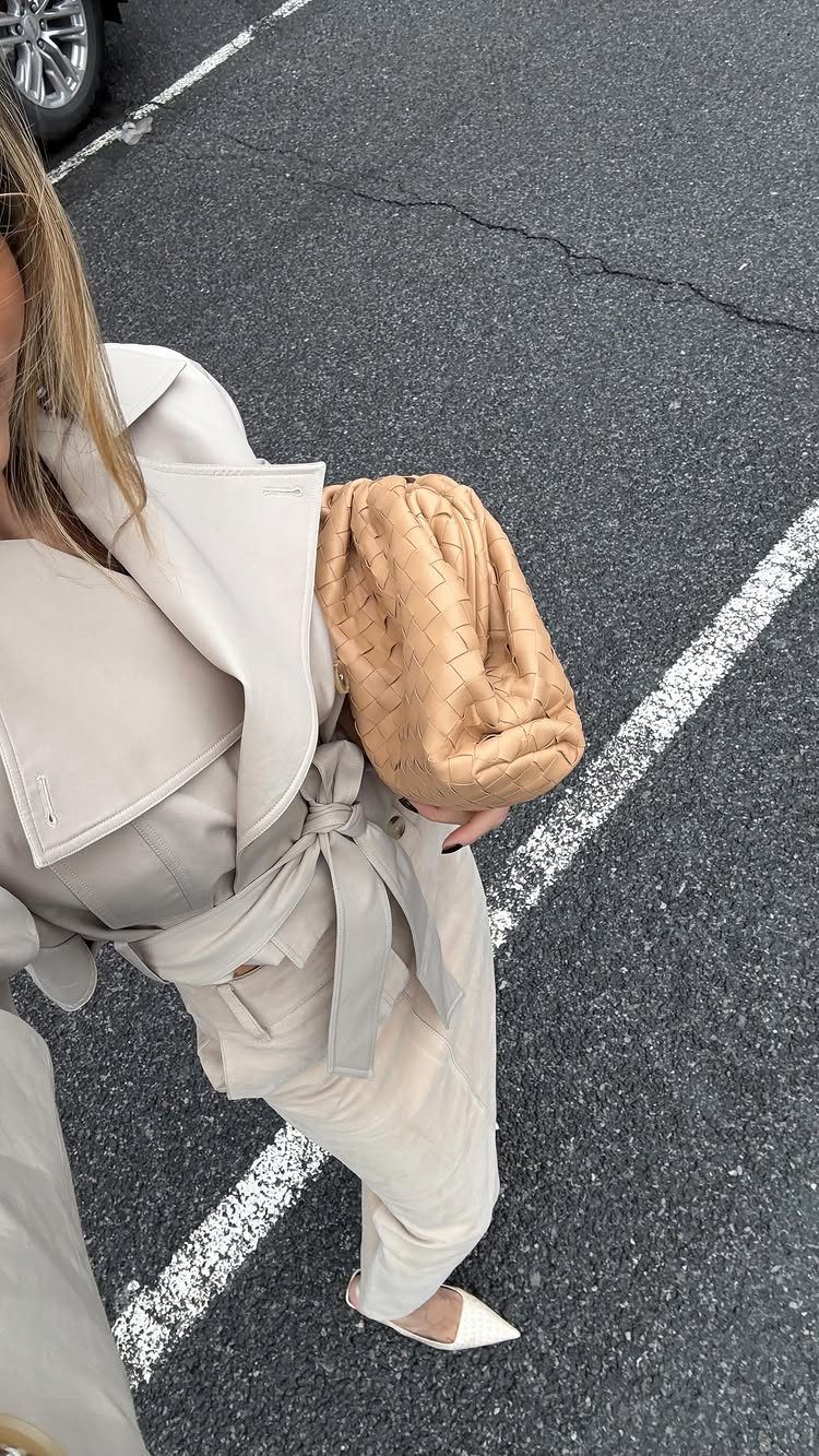 15 Trench Coat Outfit Ideas for Dressing With Intention 2 Person wearing a monochromatic beige trench coat and matching wide-leg trousers with a tan clutch.