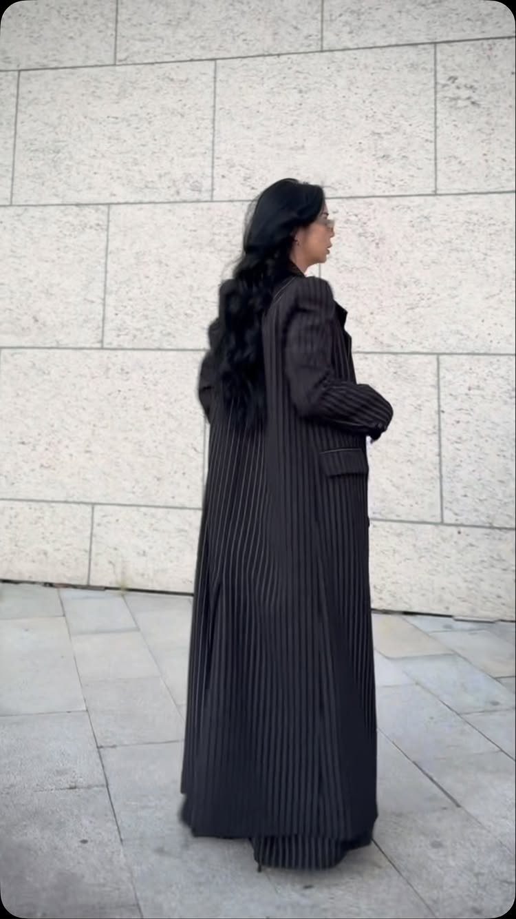 Long Jackets for Women: 8 Styles From Wool to Velvet 3 A woman wearing a long navy blue pinstripe coat standing against a stone wall.