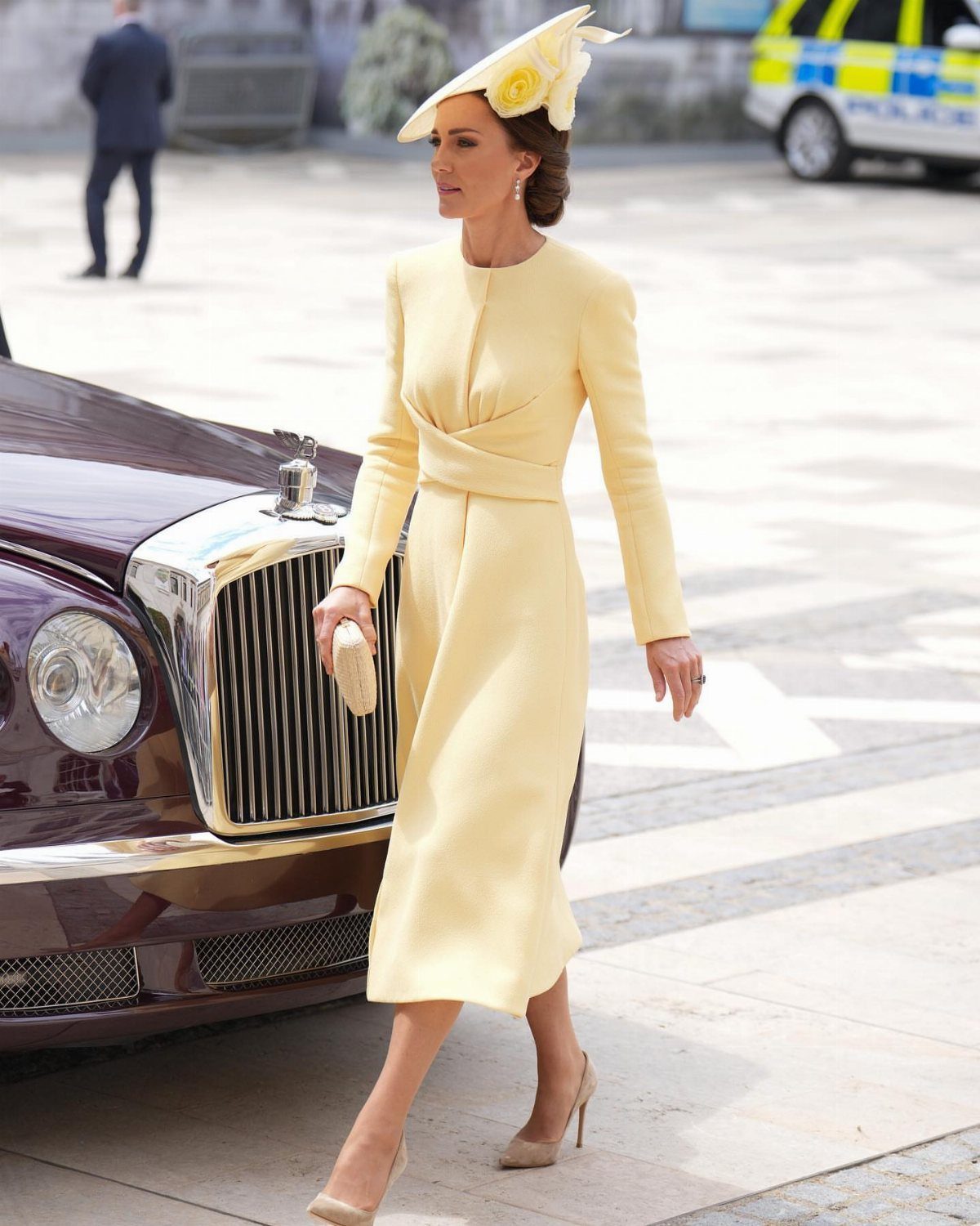 Princess Kate Outfits: 9 Style Templates to Borrow 10 Princess Kate walking in a pale yellow dress and matching fascinator near a luxury car.