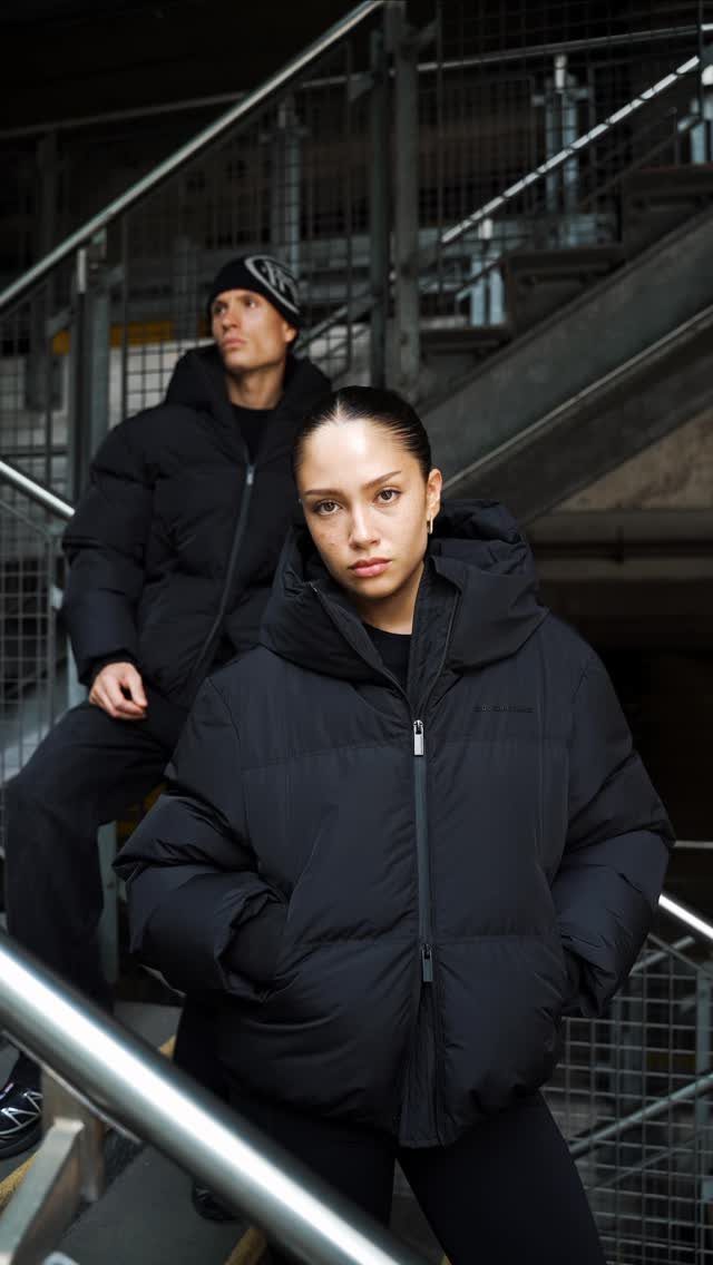 Woman wearing a large black puffer jacket and black leggings on metal stairs.