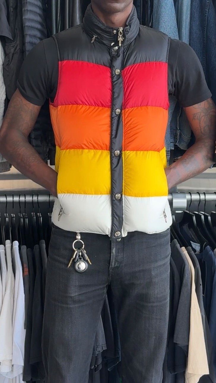 A person wearing a colorful striped puffer vest over a black t-shirt and dark jeans.