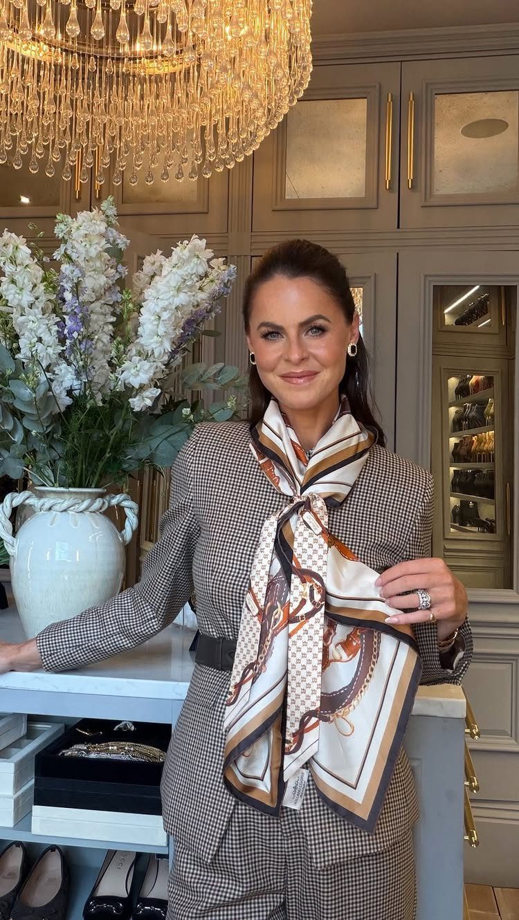 A woman wearing a patterned blazer and a large, decorative silk scarf in an elegant room.