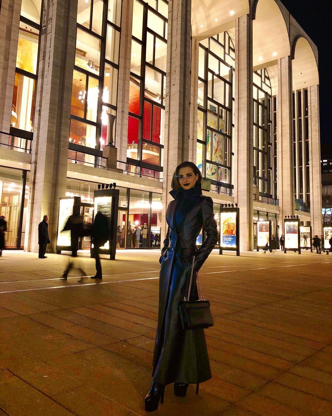 Opera Coat Women: 6 Vintage Styles Worth Wearing 7 Woman in a long dark leather opera coat standing in a plaza at night.