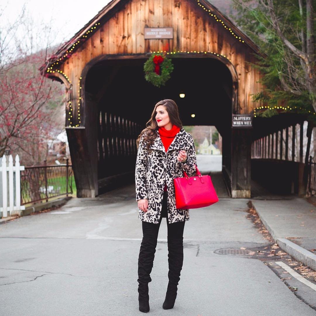 15 Long Boots Outfit Ideas for Cold Months Ahead 5 Woman wearing a patterned statement coat, red turtleneck, and black thigh-high boots standing by a covered bridge.