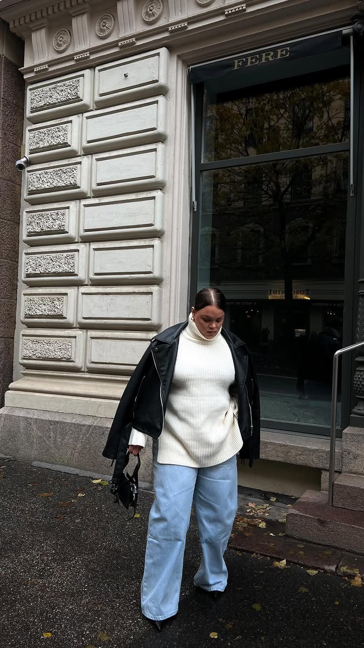 10 Knit Sweater Outfit Ideas for Fall Through Winter 2026 4 Woman wearing a white knit sweater and light blue wide-leg jeans standing outdoors.