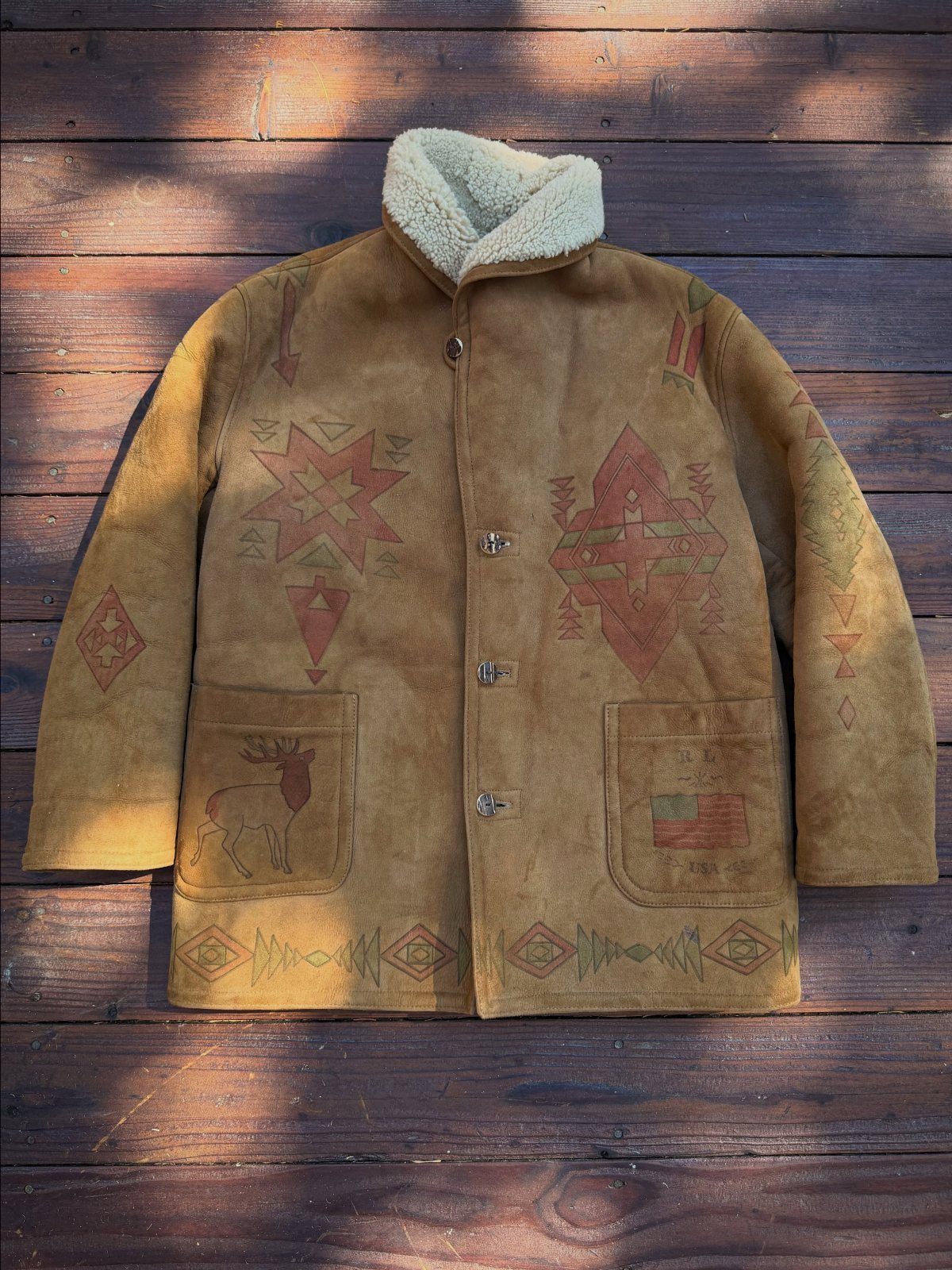 Tan suede coat with cream shearling trim and southwestern geometric patterns on a wooden background.
