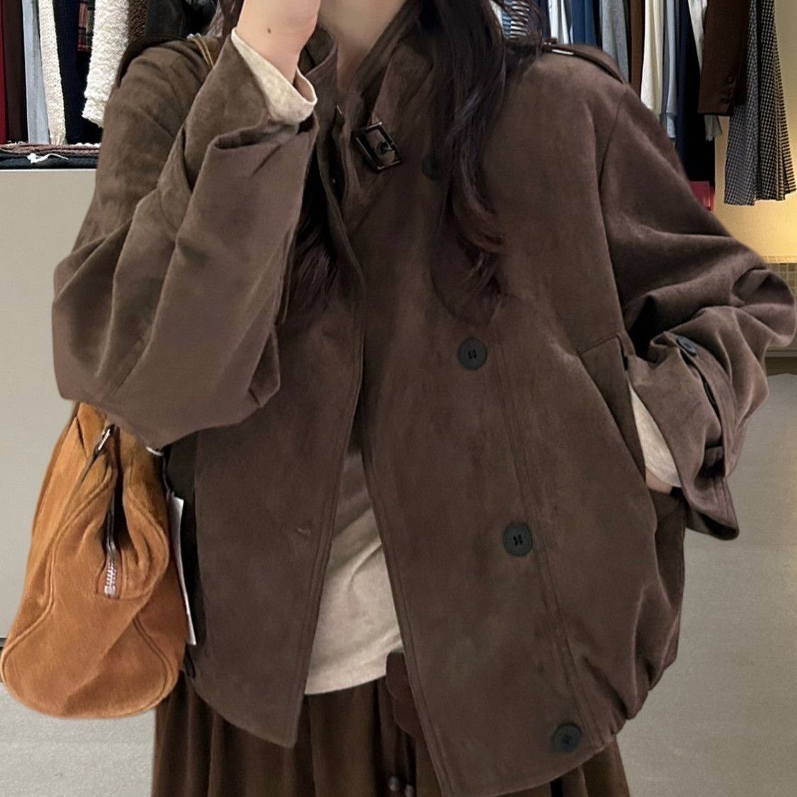 A person wearing an oversized brown suede jacket and holding a tan suede handbag.
