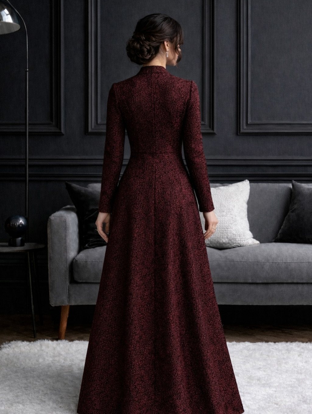 Woman in a long-sleeved burgundy floor-length gown standing in a dark room.