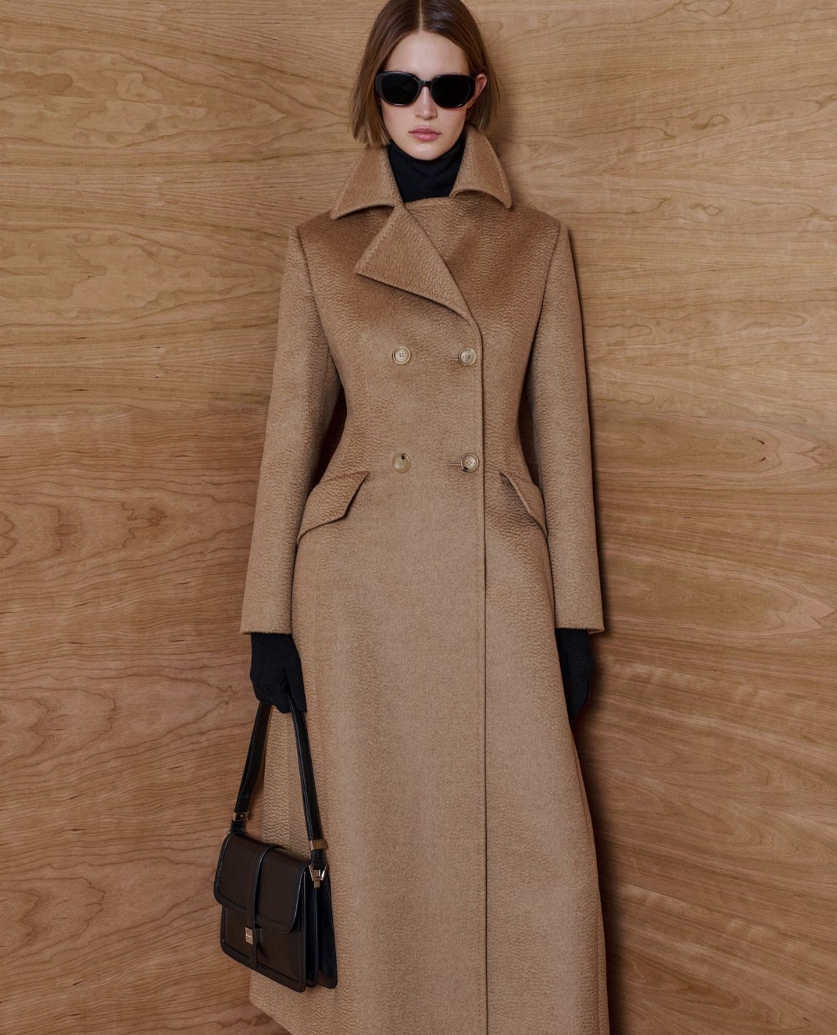 Woman posing in a long tan double-breasted wool coat and black accessories.